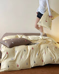 Bed with beige bedding featuring small colorful bottles, a person standing in the background.