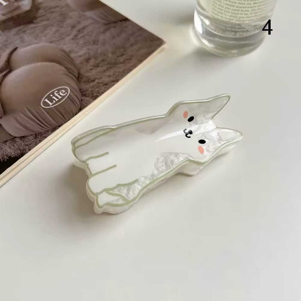 A group of colorful acetate cat hair claw clips in various cartoon designs resting on a beige ceramic plate