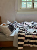 Bed with black and white striped bedding and pink accents, near a window.