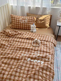 Brown checkered bedding set with 'Puppy' embroidery on a bed in a bright room.