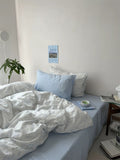 Bedroom with light blue bedding and pillows, a plant, and a calendar on the wall.