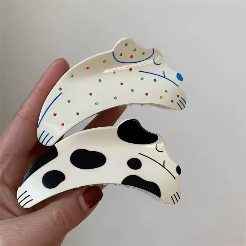 Overhead image showing all color variants of the dog-shaped claw clip, including tortoiseshell, black-and-white, camo green, and rhinestone polka dot styles