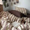 Bed with striped bedding and pillows, book, and cup on a wooden floor.