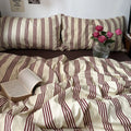 Bed with striped bedding, open book, and vase of flowers on a wooden nightstand.