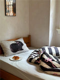 Bed with zebra-patterned blanket and pillow featuring a black cat design, in a room with neutral walls and a window.
