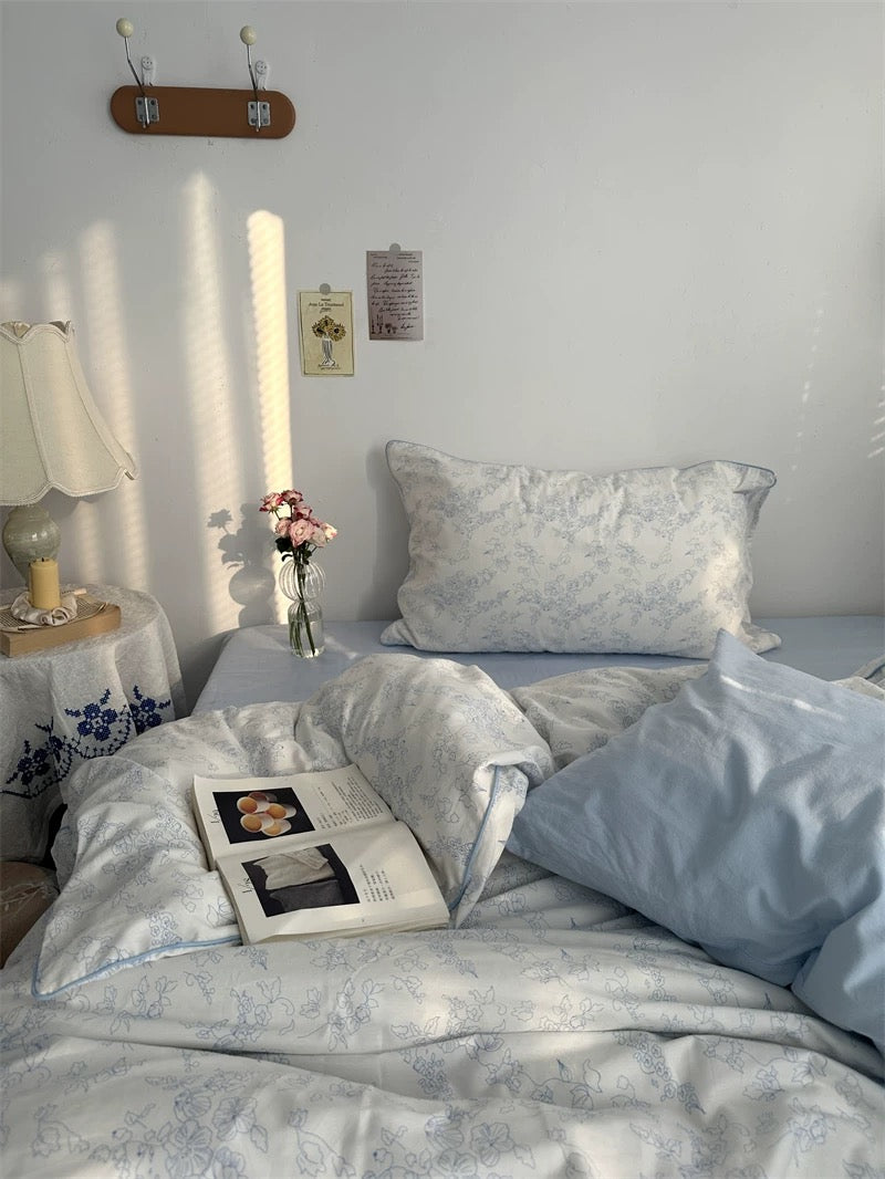 Bedroom with light blue bedding, a book, and a vase on a nightstand.