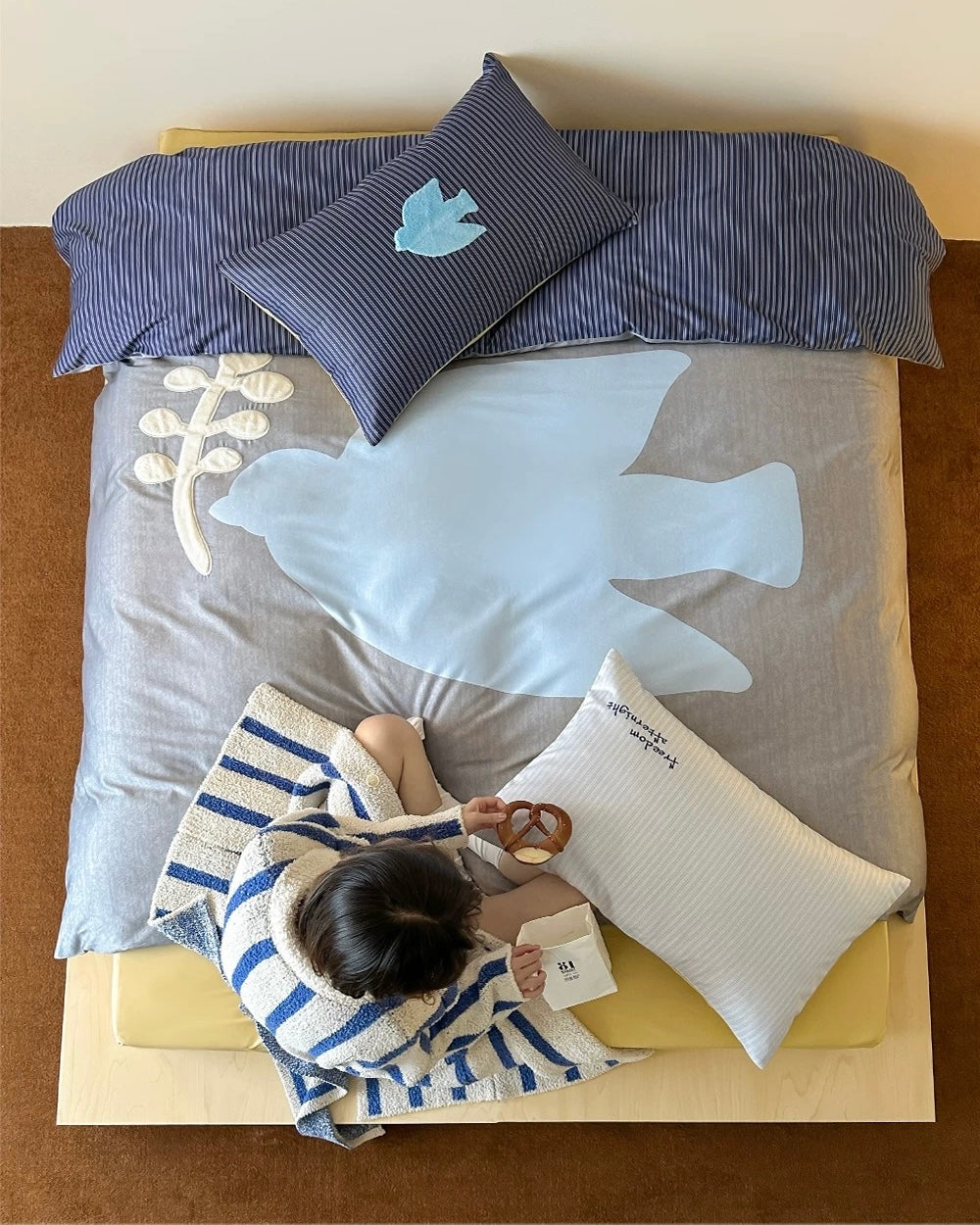 Person lying on a bed with blue and gray bedding, holding a phone.