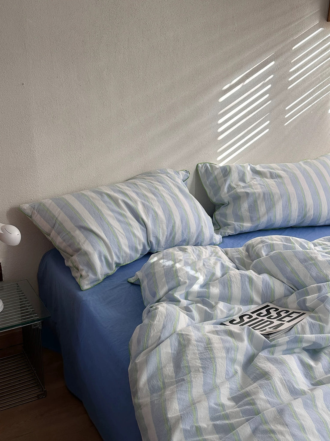 Bed with striped bedding and green pillow, nightstand with lamp and plate.