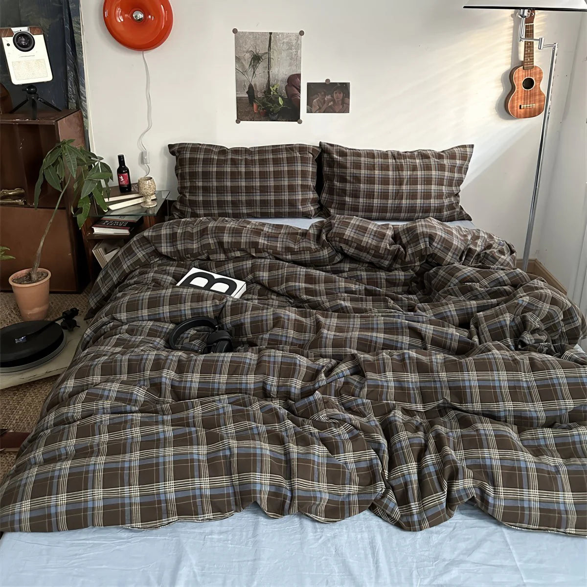 Bedroom with plaid bedding, guitar, and decor items on a white wall.