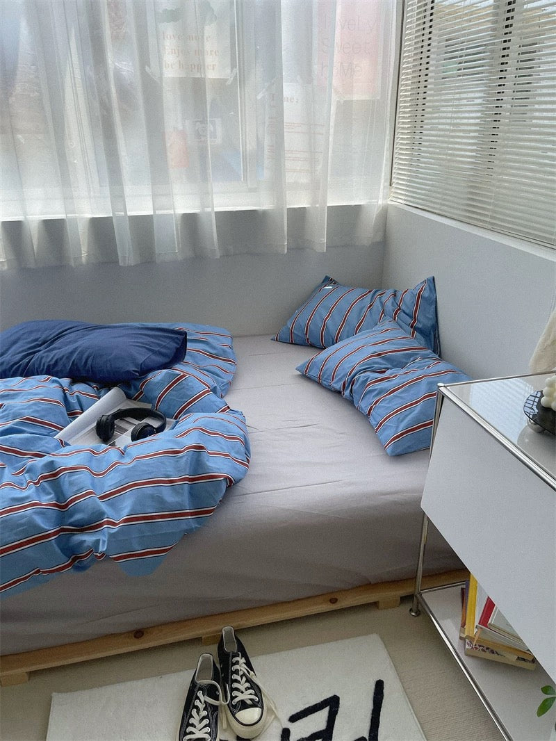 Bed with blue striped bedding and pillows in a room with a desk and window.