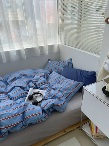 Bed with blue striped bedding in a room with white curtains and a nightstand.