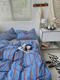 Bedroom with blue striped bedding, nightstand, and window blinds.
