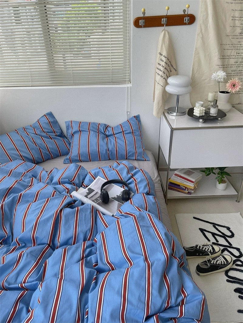 Bedroom with blue striped bedding, nightstand, and window blinds.