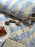 Striped pillow with bow design on a bed with a plate of food and book.