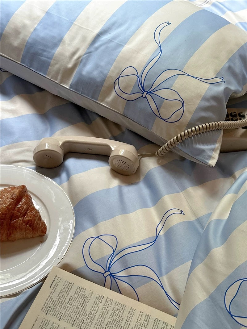 Striped pillow with bow design on a bed with a plate of food and book.