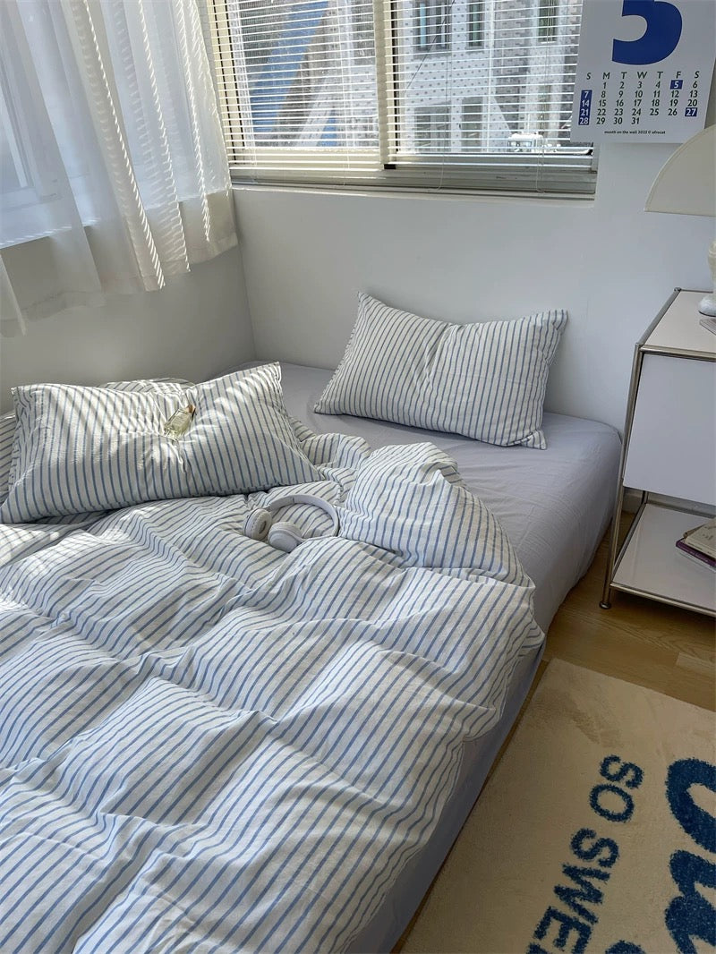 Bedroom with a neatly made bed featuring striped bedding and pillows, next to a window with blinds.