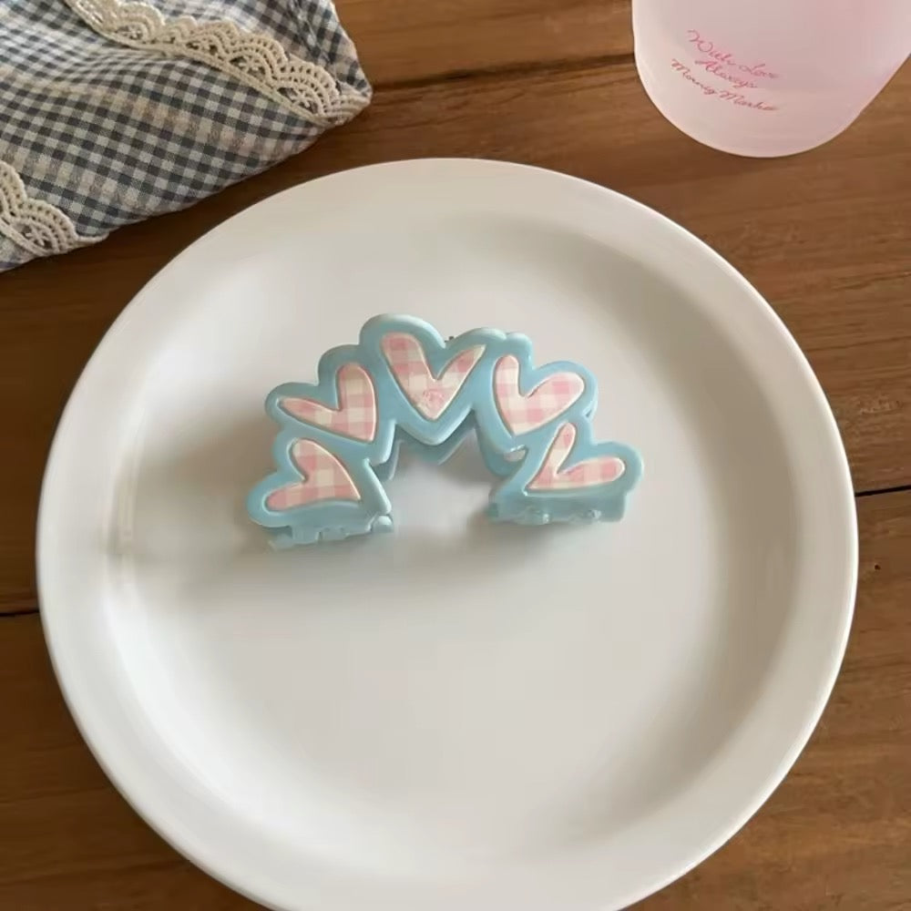 Pink gingham triangle acrylic hair claw clip with tiny blue bow detail, set beside pearls and accessories