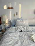 Bedroom with light blue bedding and a lamp on a nightstand.