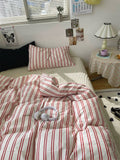Bed with red and white striped bedding in a room with a small table and lamp.