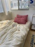 Bed with white bedding and red pillows near a window with blinds.