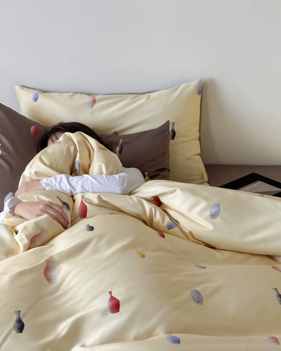 Person lying in bed under a yellow comforter with small decorative items on pillows.