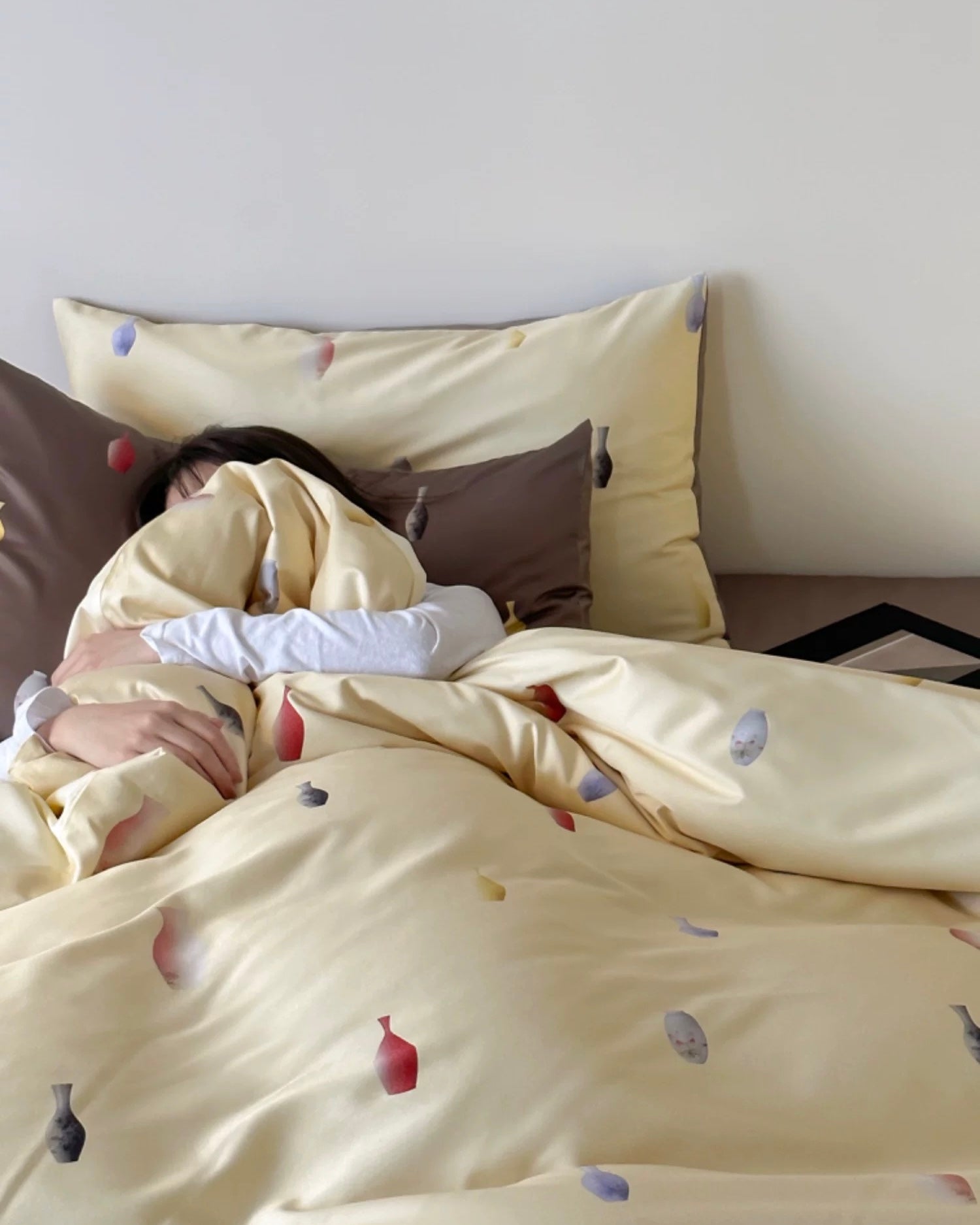 Person lying in bed under a yellow comforter with small decorative items on pillows.