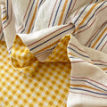 Close-up of fabric with yellow checkered, white, orange, and blue striped patterns.