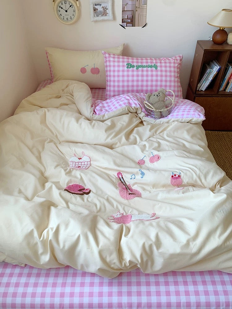 Bed with pink checkered sheets and white comforter, featuring a teddy bear and books on a nightstand.