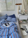 Bedroom with blue striped bedding, white nightstand, and window blinds.
