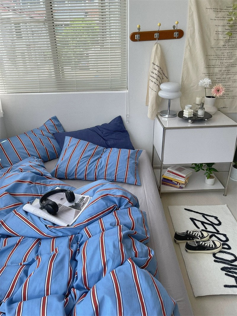 Bedroom with blue striped bedding, white nightstand, and window blinds.