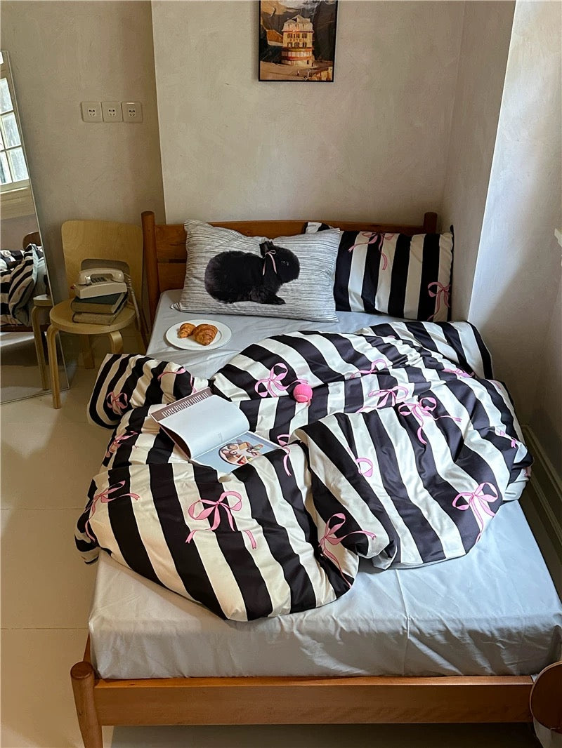 Bed with striped bedding and decorative pillows in a room with a chair and table.