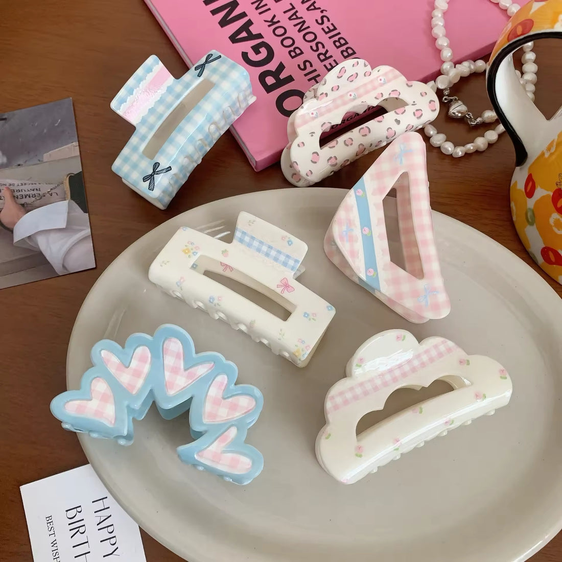 Five coquette-style hair claws laid out on a ceramic plate in a color-coordinated flat lay