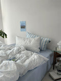 Bedroom with light blue bedding and striped pillows, a plant, and a magazine on the wall.