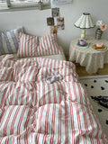 Bed with red and white striped bedding in a room with a small table and lamp.
