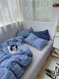 Bed with blue striped bedding and pillows in a bright room.