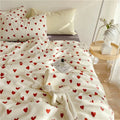 White comforter with red heart pattern on a bed in a bedroom setting.