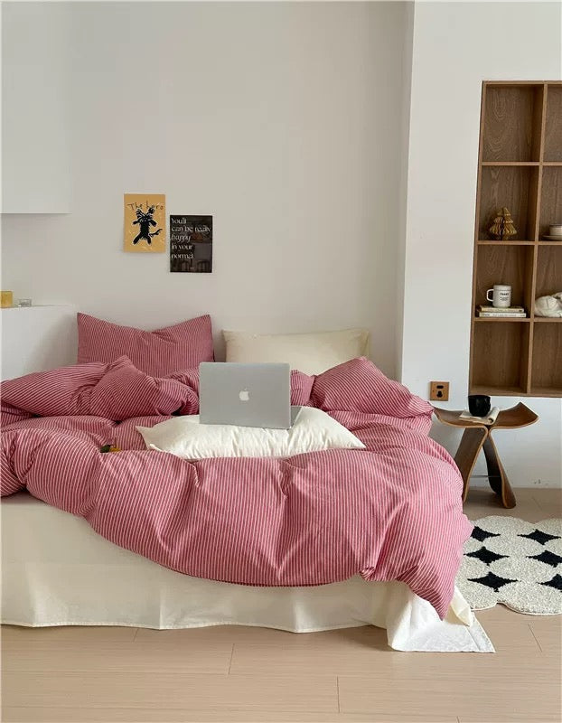 Bed with pink comforter and laptop, wooden shelf in the background