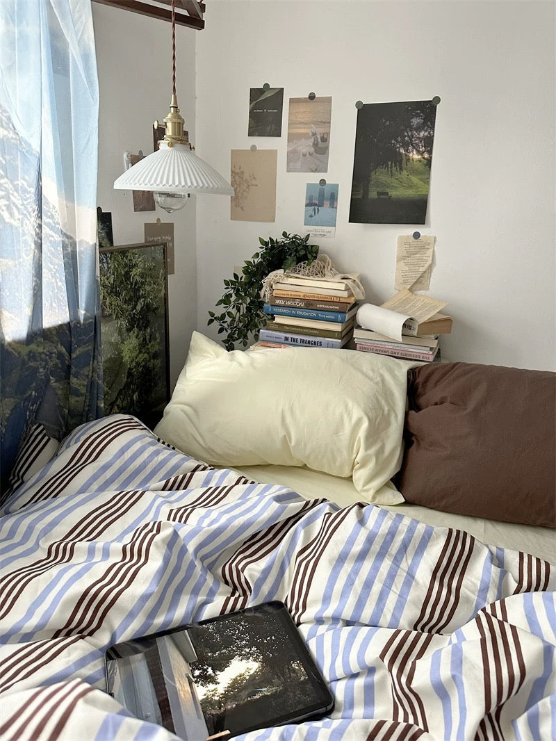 Bedroom with striped bedding, pillows, and a laptop on a nightstand.