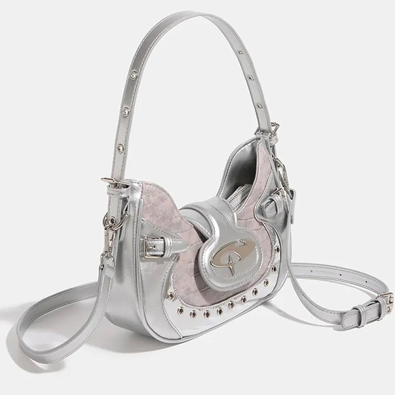 Y2K crescent-shaped shoulder and crossbody bag in silvery pink with crocodile texture, punk-inspired details and metal rivets for edgy 2000s fashion outfits