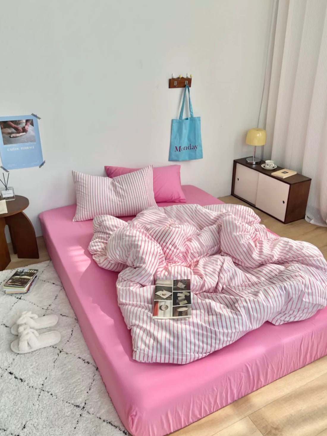 Pink bed with striped bedding in a room with a lamp and shelves.