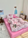 Pink bed with striped bedding in a room with a lamp and shelves.