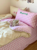 Bed with pink checkered bedding, teddy bear, and pillow with 'Be yourself' text.