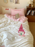 Bed with pink checkered pillowcases, cartoon character pillow, and teddy bear on a bedspread.