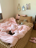 Bed with pink comforter and plaid blanket, pillows, and a clock on the wall.