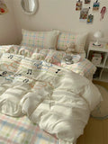 Bedroom with white comforter featuring musical notes, checkered bedspread, and decorative pillows.