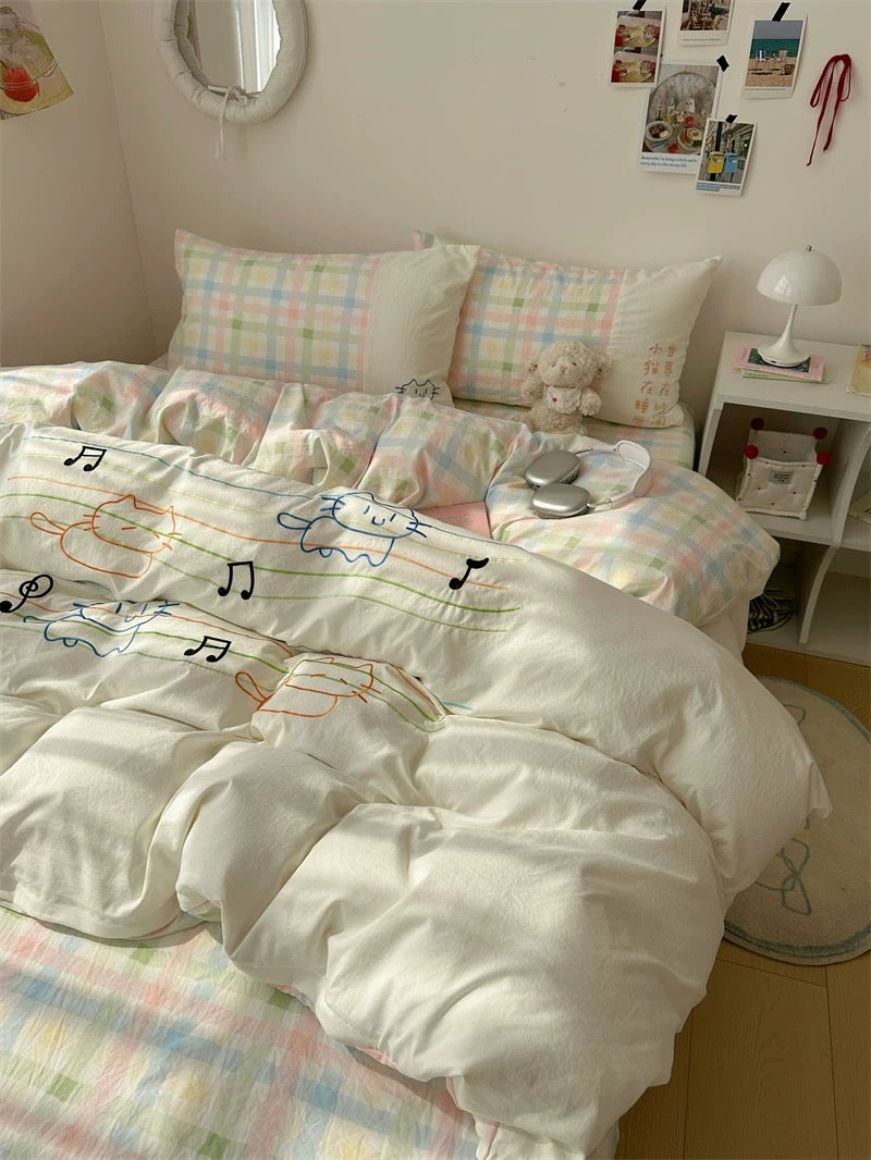 Bedroom with white comforter featuring musical notes, checkered bedspread, and decorative pillows.
