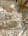 Floral patterned bedspread and pillow on a bed with a rug and slippers in the background.