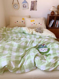 Bed with green checkered blanket featuring a cartoon character, pillows with face designs, and a nightstand with books.
