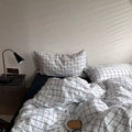 Bed with grid-patterned bedding and pillows in a room with a lamp and nightstand.