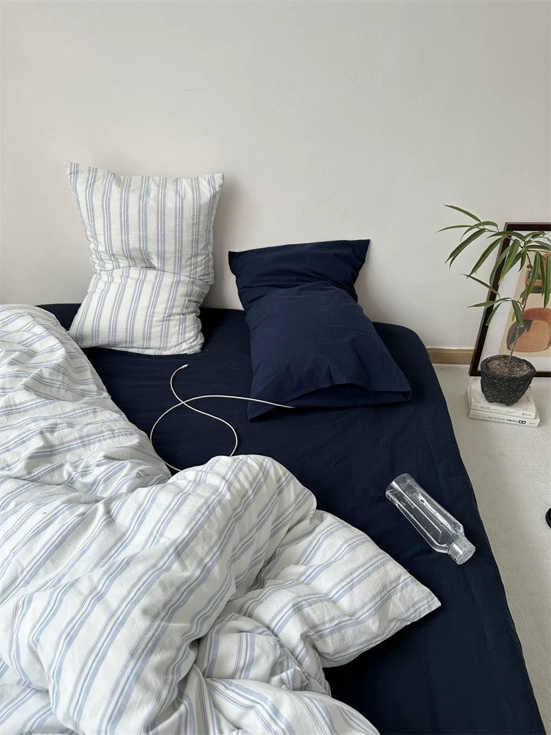 Bedroom with striped bedding, photos on the wall, and a plant.